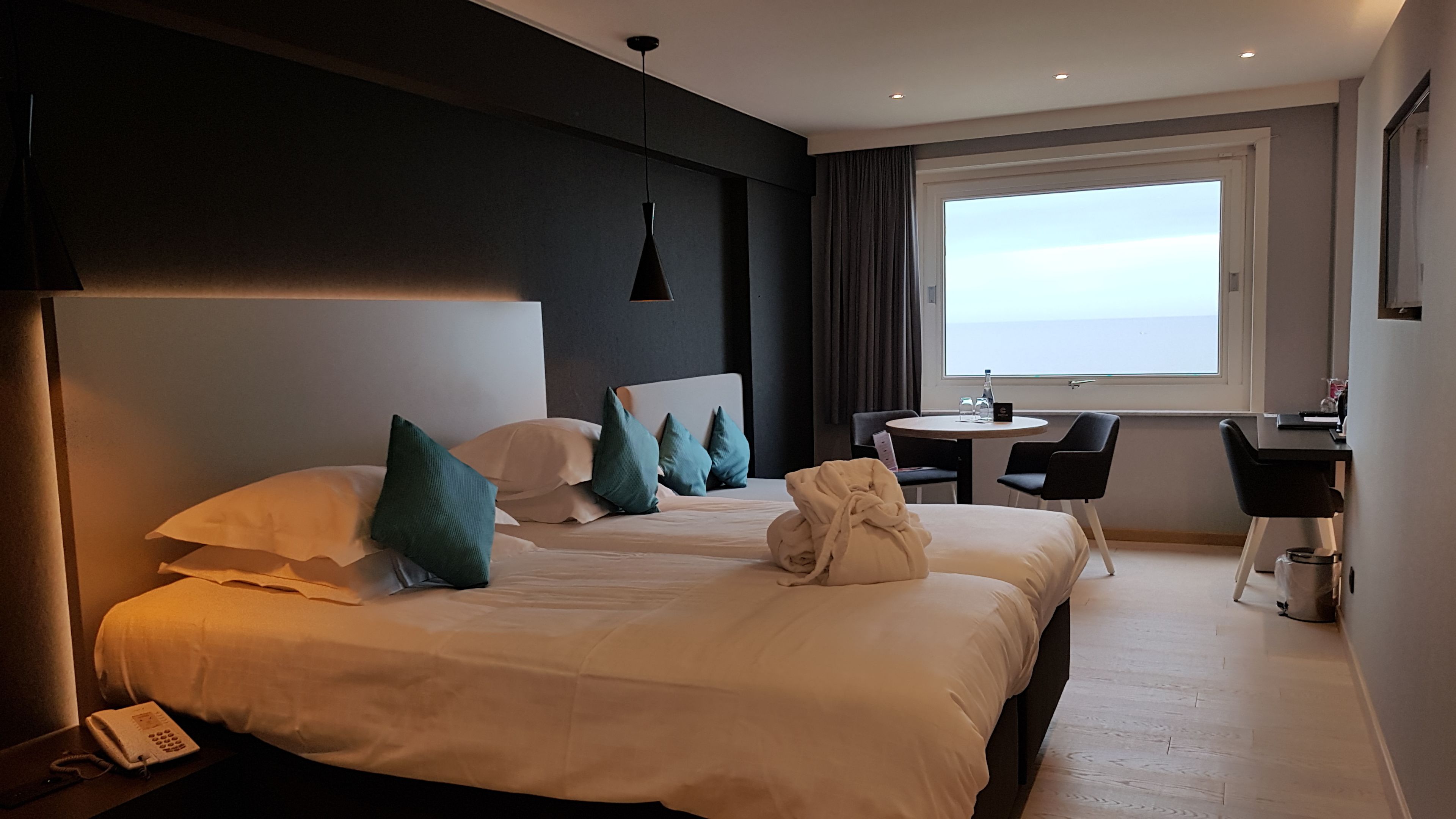 A hotel room with a large bed, a desk, and a view of the sea.