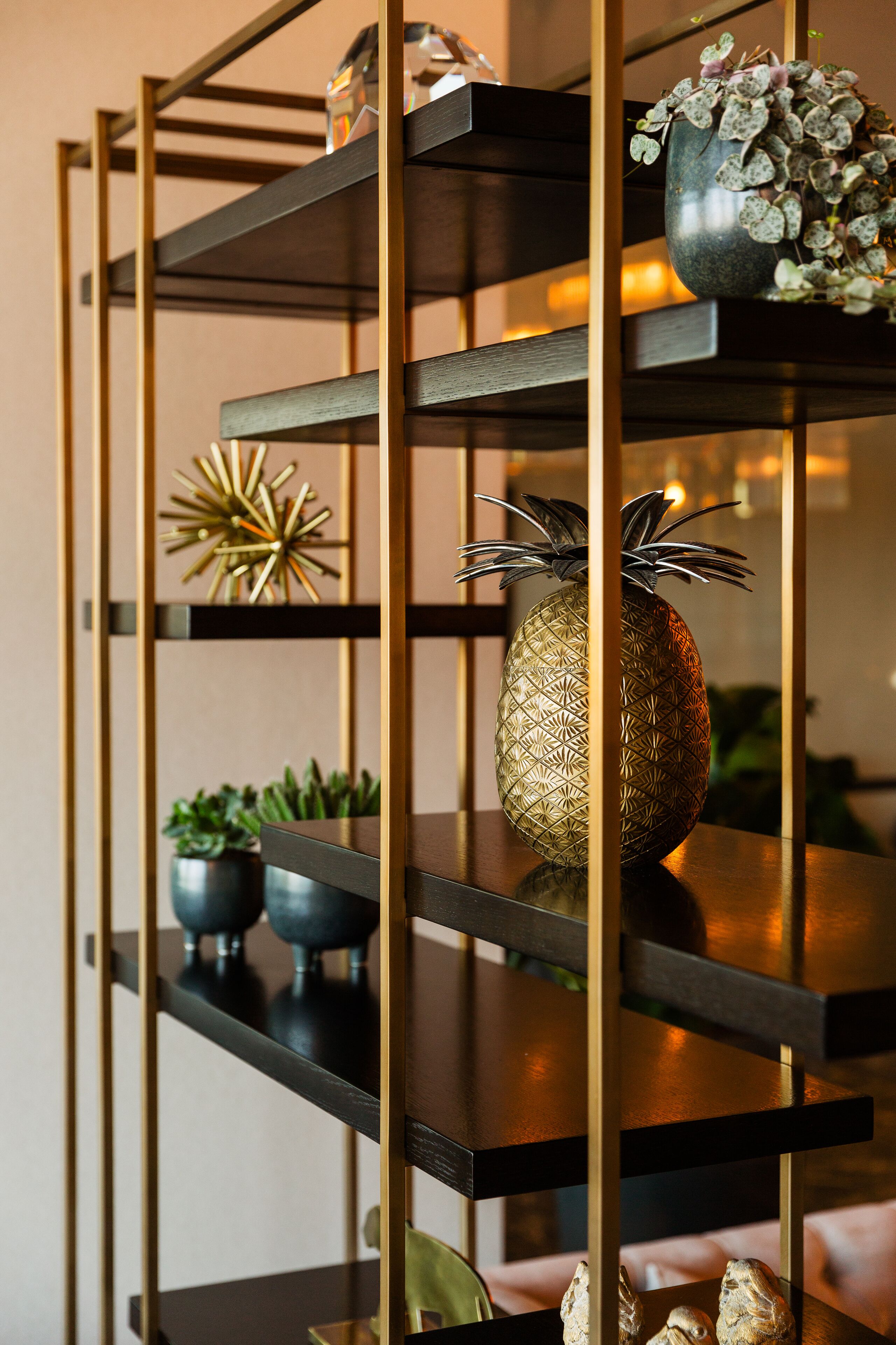 A wooden shelving unit with decorative items including a pineapple-shaped vase and a geometric sculpture.