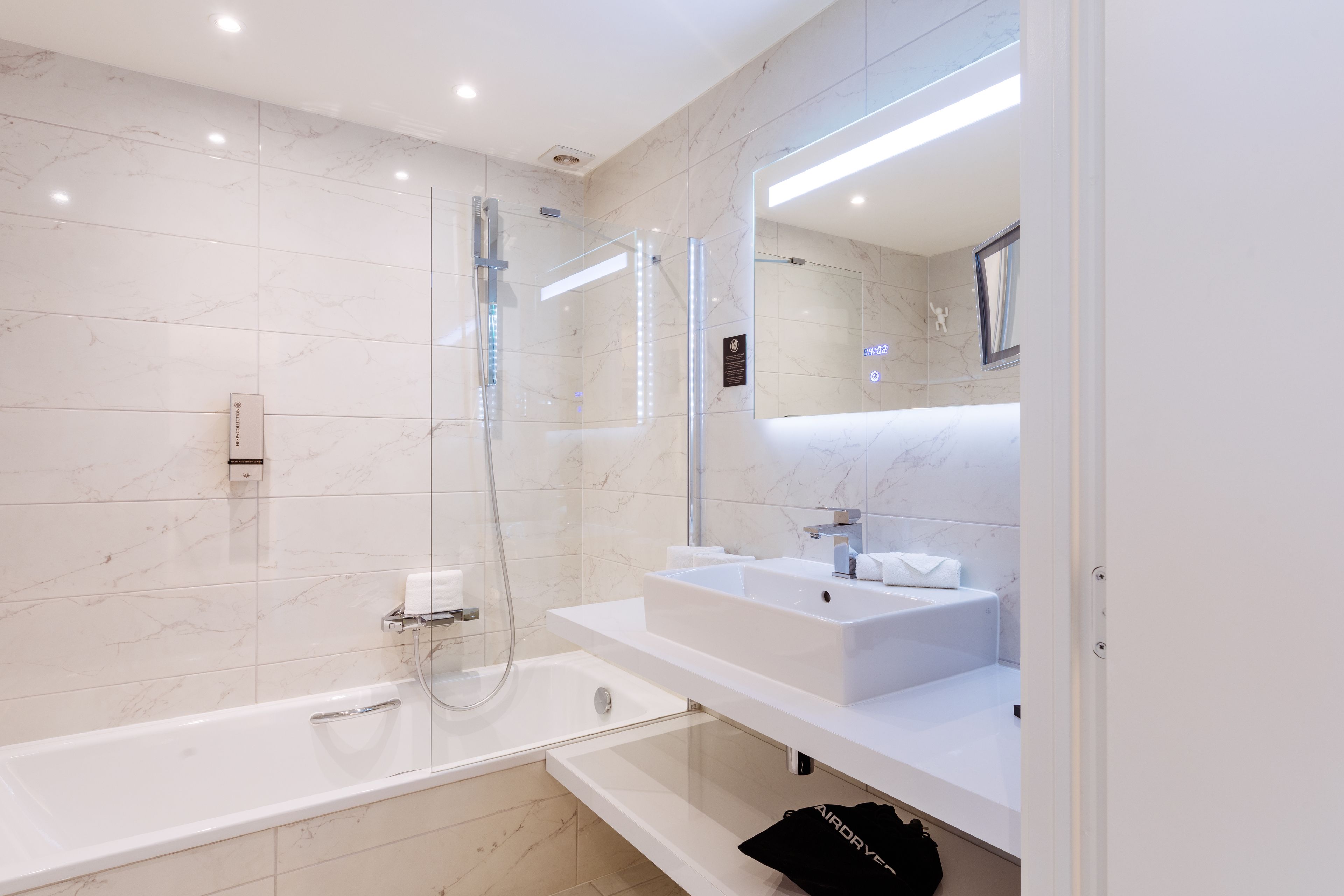 Ein modernes Badezimmer mit einer Glaskabine zur Dusche, einem weißen Waschbecken und einem großen Spiegel.