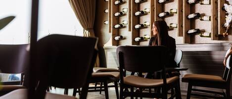 L’intérieur d’un restaurant, avec un mur entièrement recouvert de bouteilles de vin, des chaises en bois et un lustre moderne.