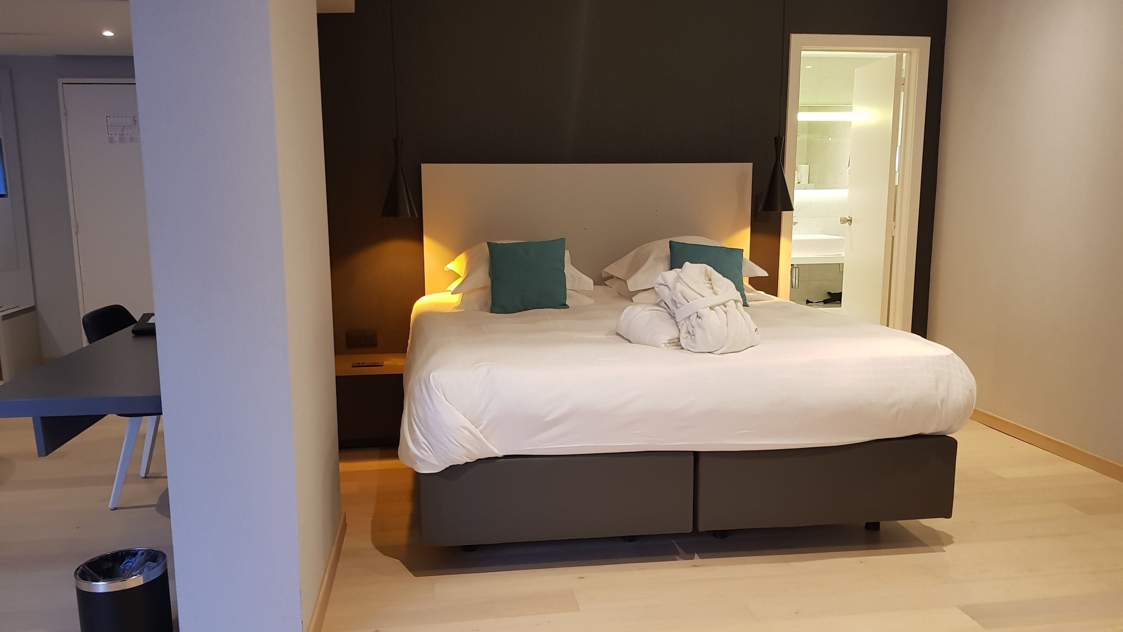 Une chambre d’hôtel moderne équipée d’un grand lit, d’une table de chevet, d’un bureau et d’une poubelle.