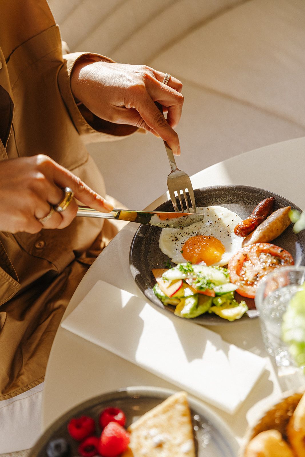 Une personne est assise à table et mange un plat composé d’œufs, de bacon et de légumes.