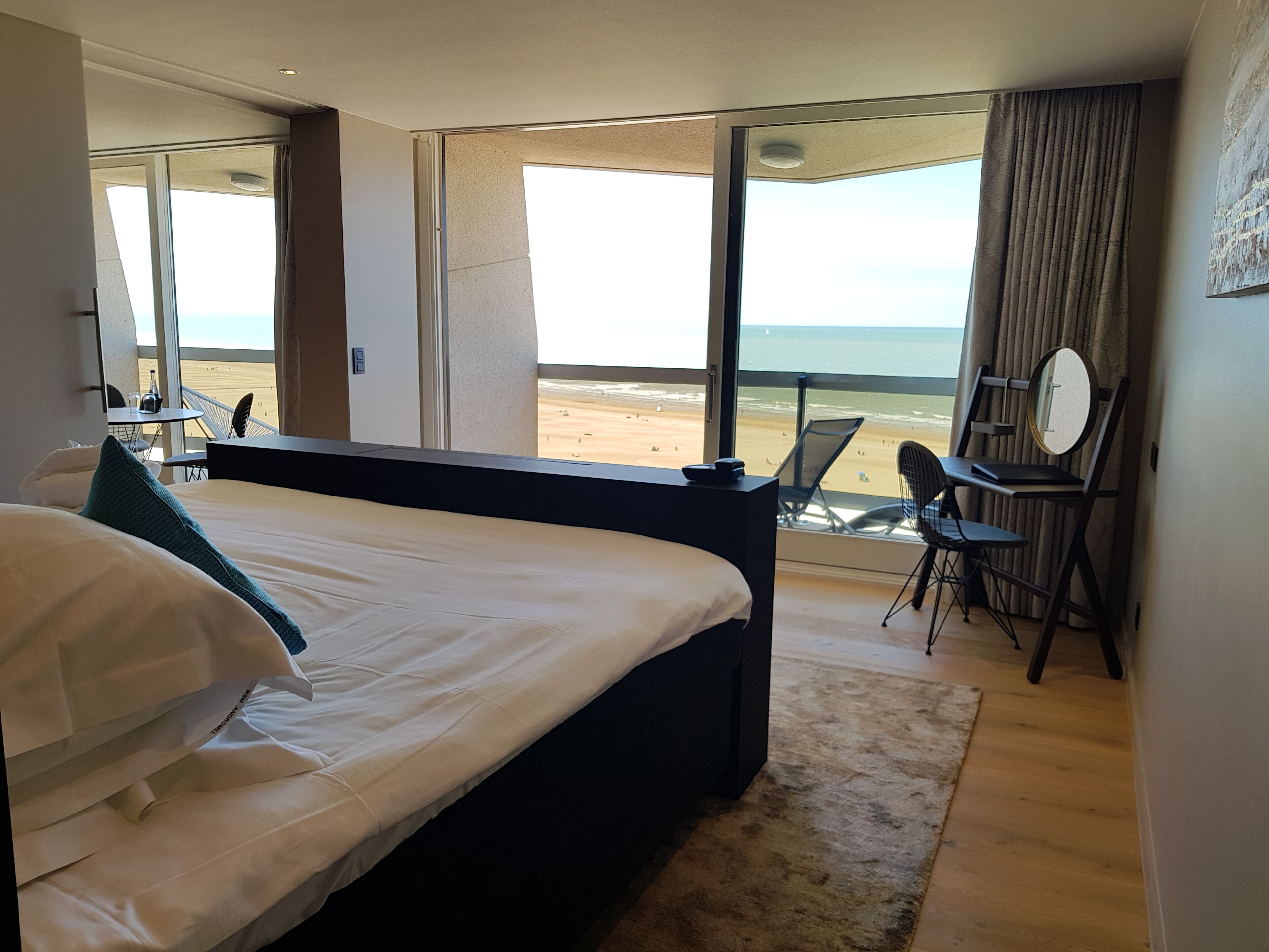 A hotel room with a large bed, a desk, a chair, and a view of the beach.
