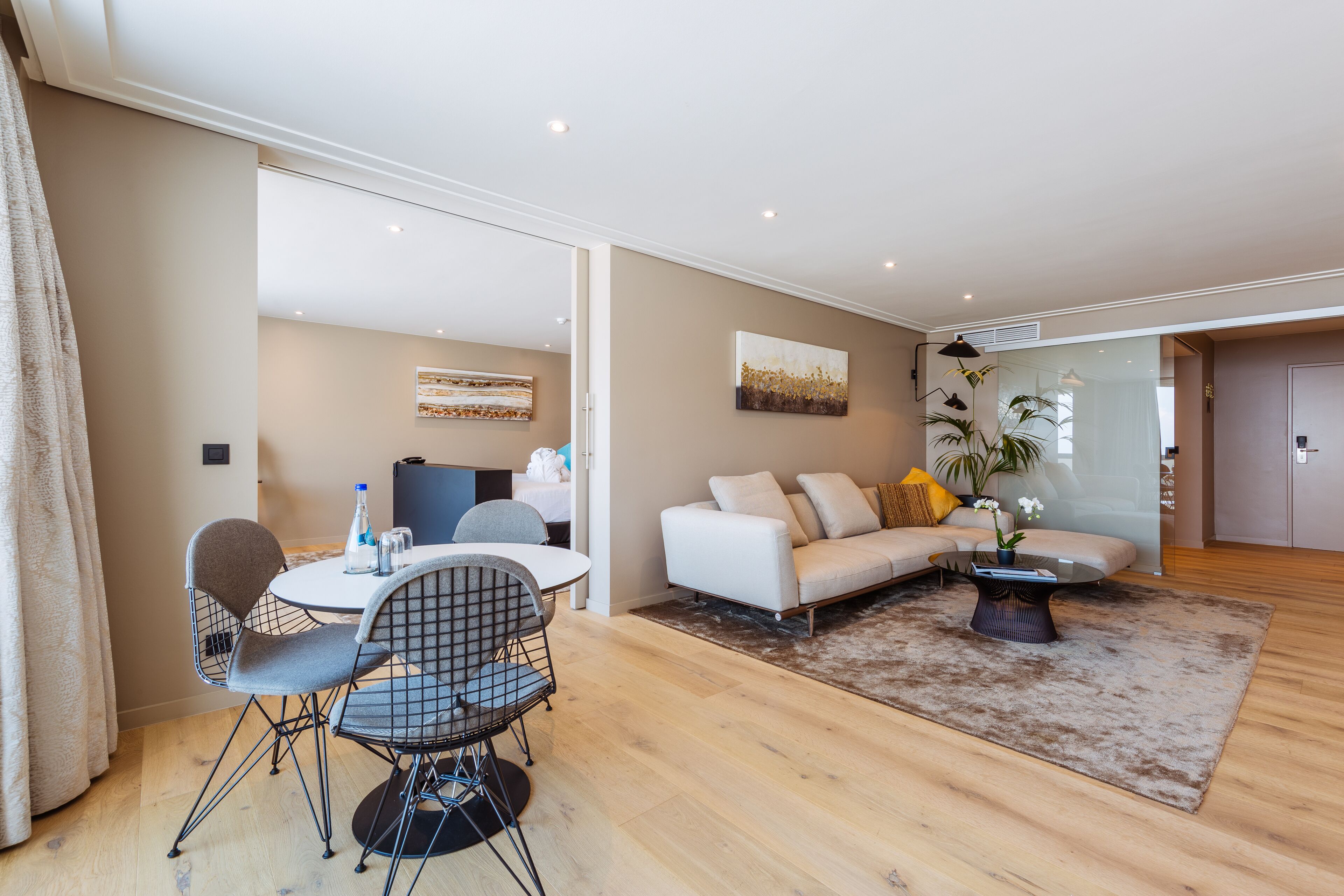 Una sala de estar moderna con un sofá blanco, una mesa de comedor redonda con sillas y una mesita de centro con una planta.