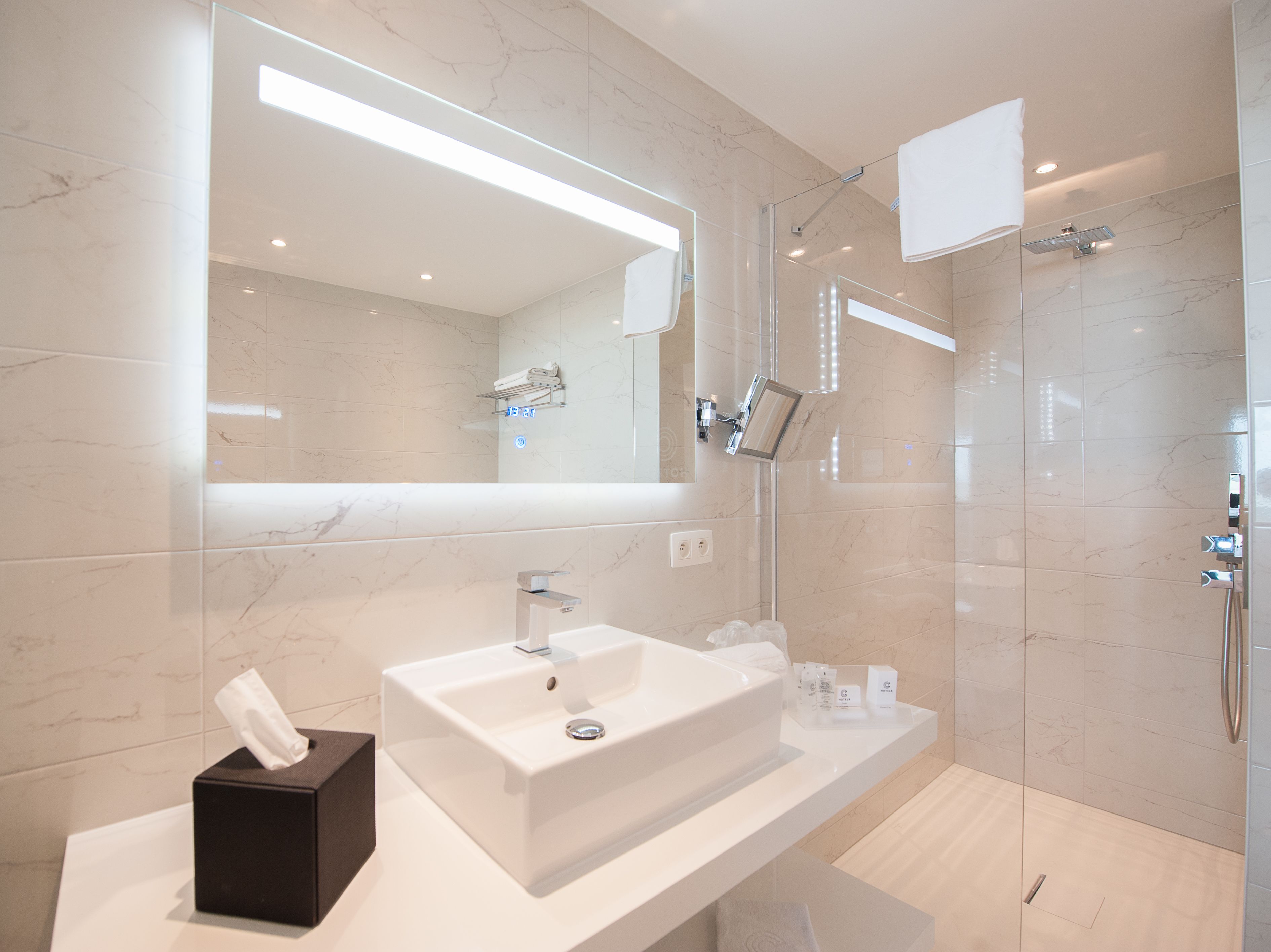 A modern bathroom with a large mirror, a white sink, a glass shower enclosure, and a towel rack.