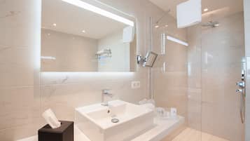 A modern bathroom with a large mirror, a white sink, a glass shower enclosure, and a towel rack.