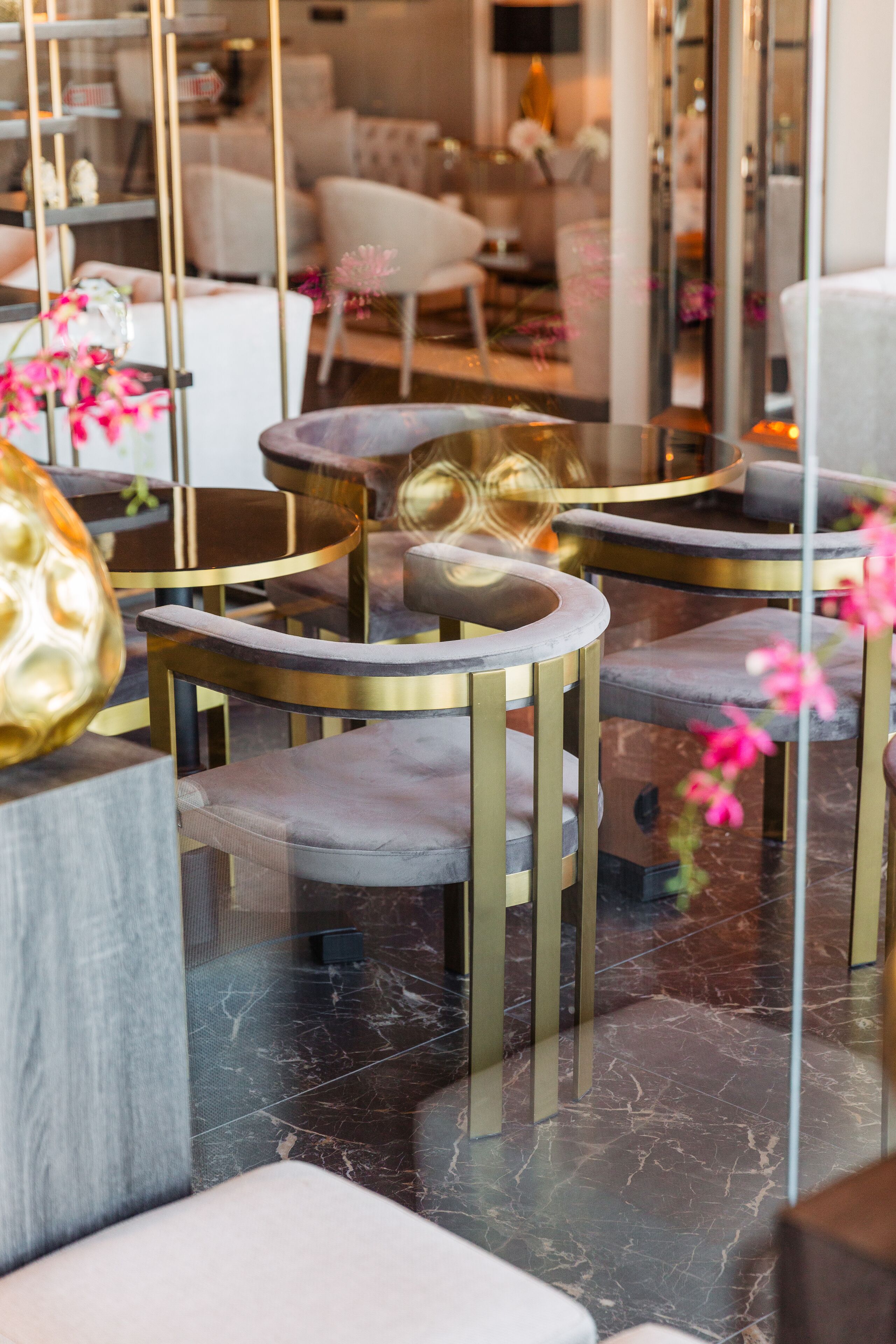 A modern interior with round tables and chairs, marble flooring, and a glass partition reflecting the room.
