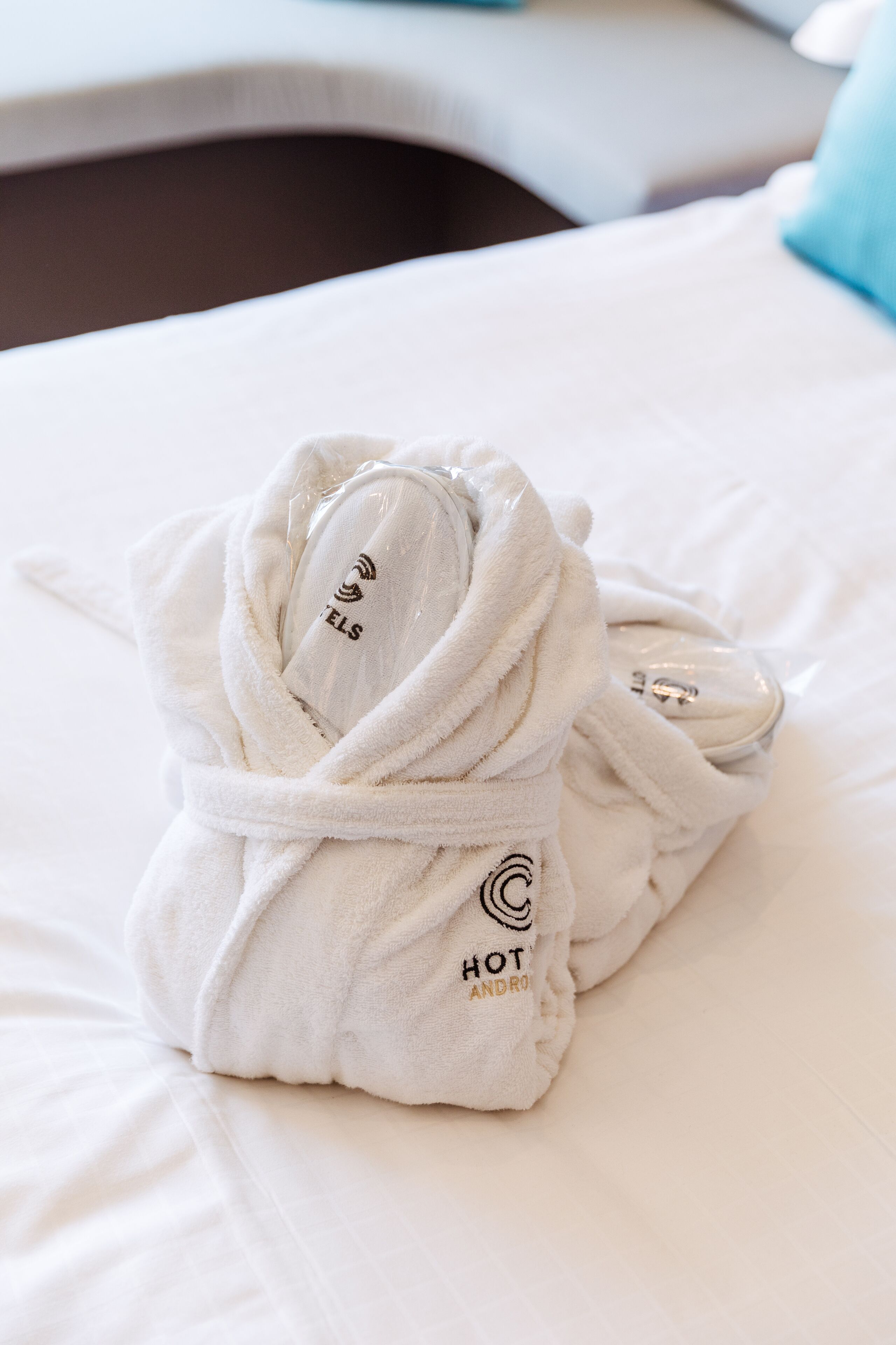 A neatly folded white bathrobe with "HOT ANDRO" text and a logo on a bed.