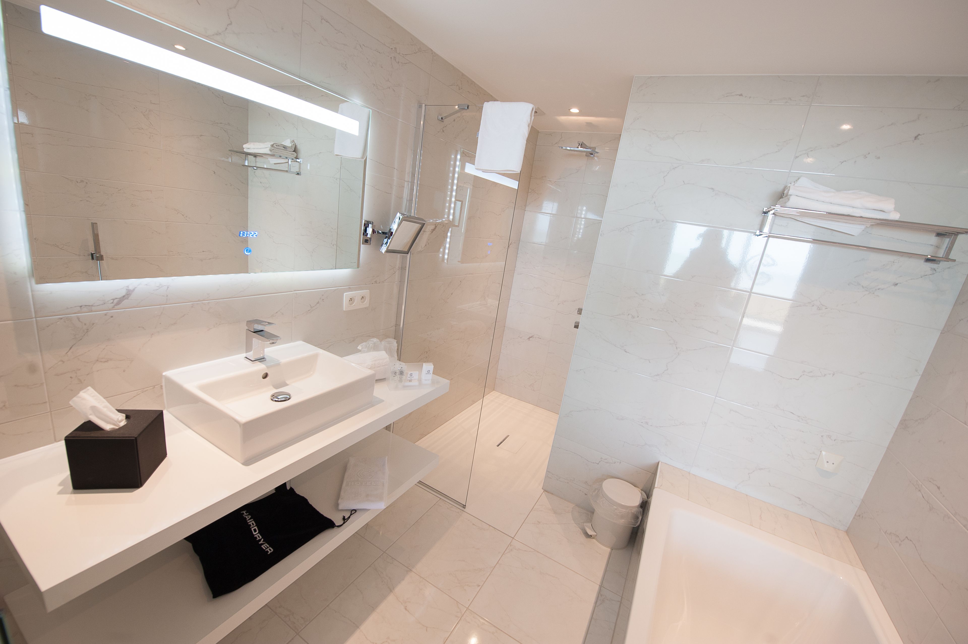 A modern bathroom with a large mirror, white sink, and a glass-enclosed shower.