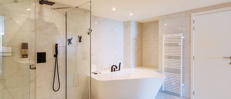 A modern bathroom with a glass-enclosed shower, a freestanding bathtub, and a white towel rack.