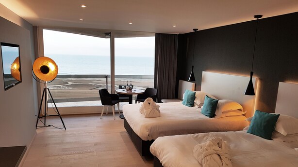 Une chambre d’hôtel avec deux lits, un coin repas et une grande fenêtre donnant sur la plage.