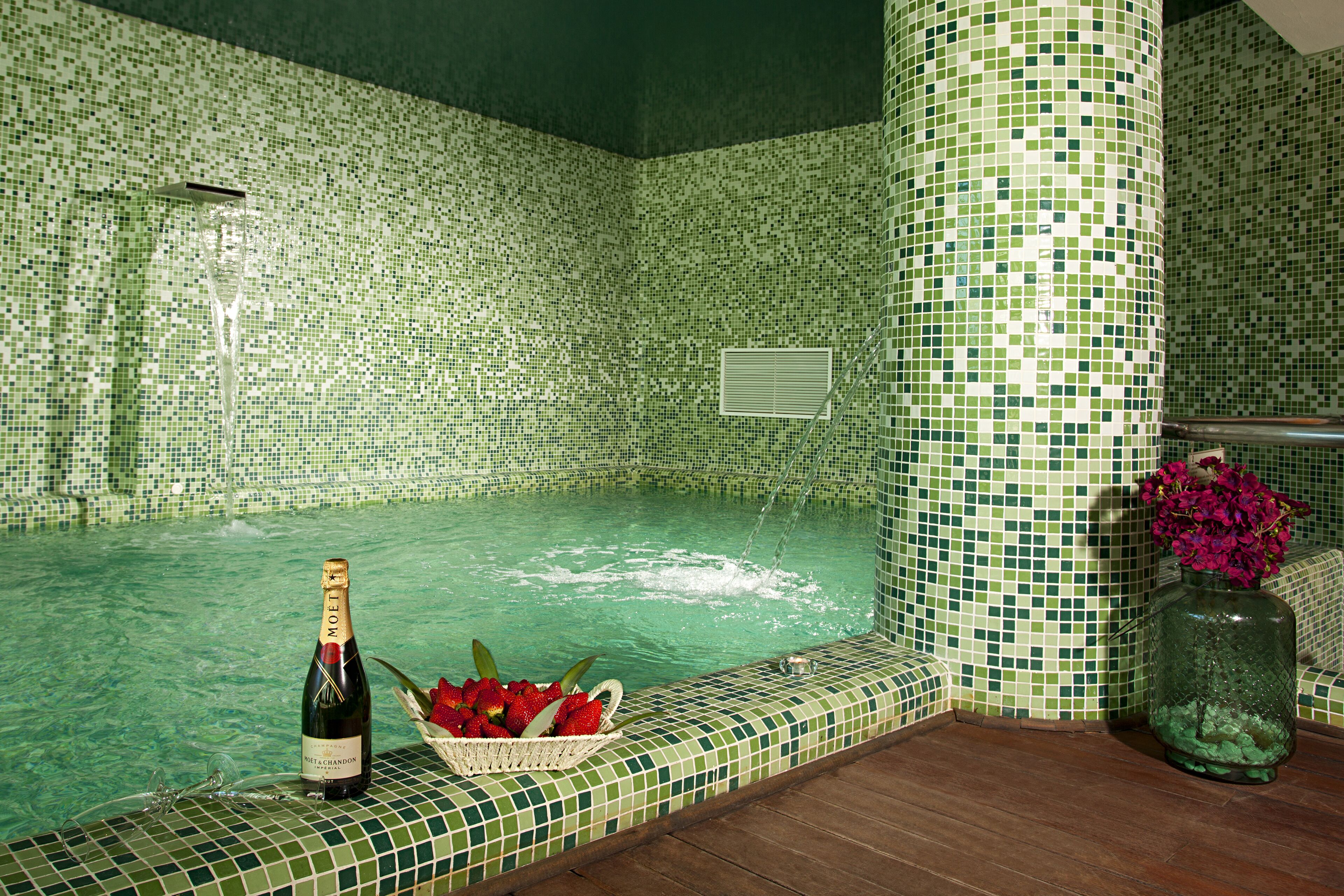 A tiled jacuzzi with a bottle of champagne and a basket of strawberries.