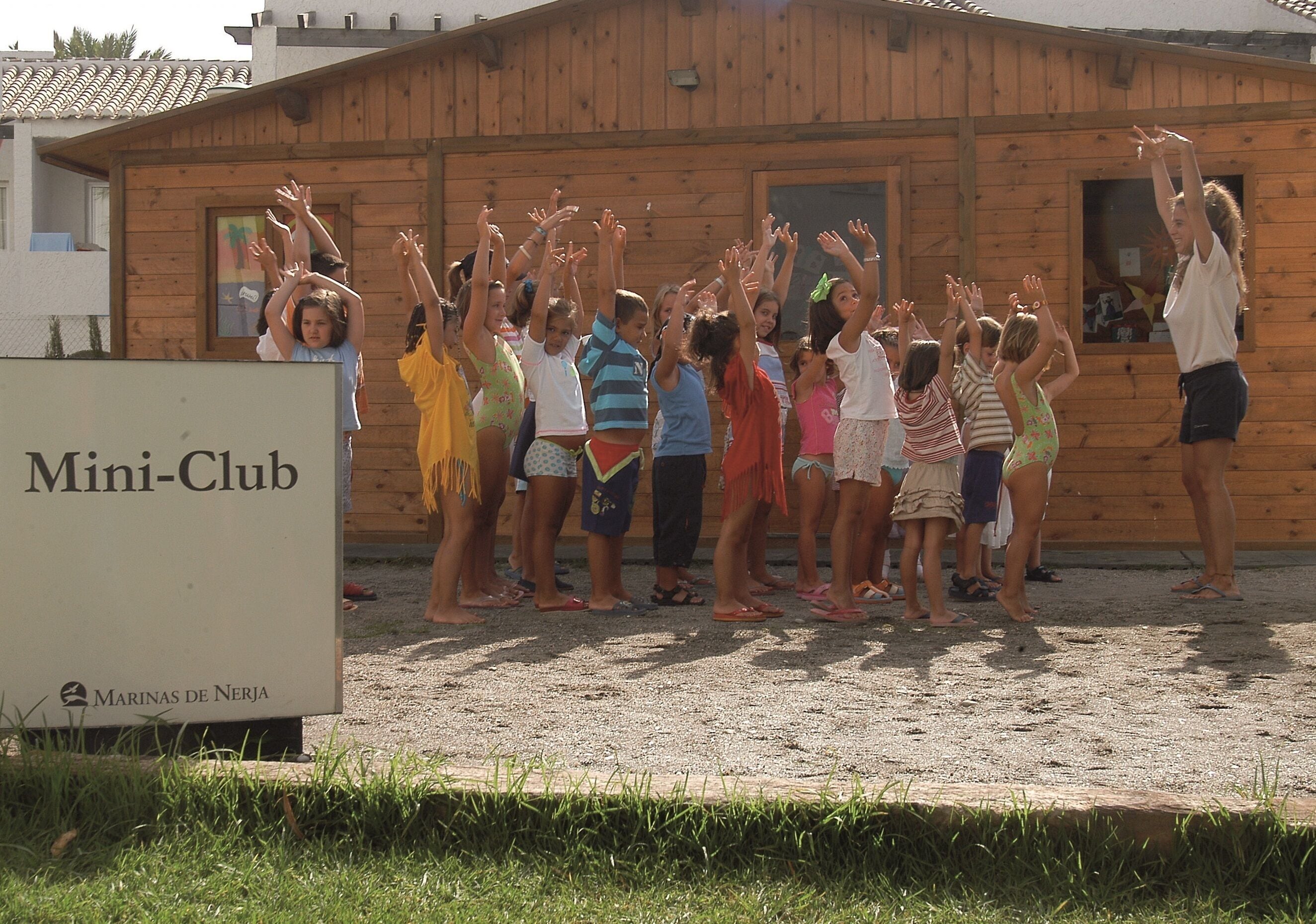 Un groupe de personnes se tient devant un bâtiment en bois sur lequel est apposée une enseigne indiquant « Mini-Club ».