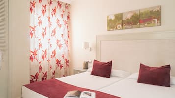 A hotel room with a bed, a nightstand, a lamp, and a window with curtains.