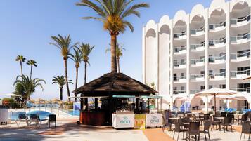 Un área de piscina en un resort, con sillones de descanso, un bar y un edificio con balcones.