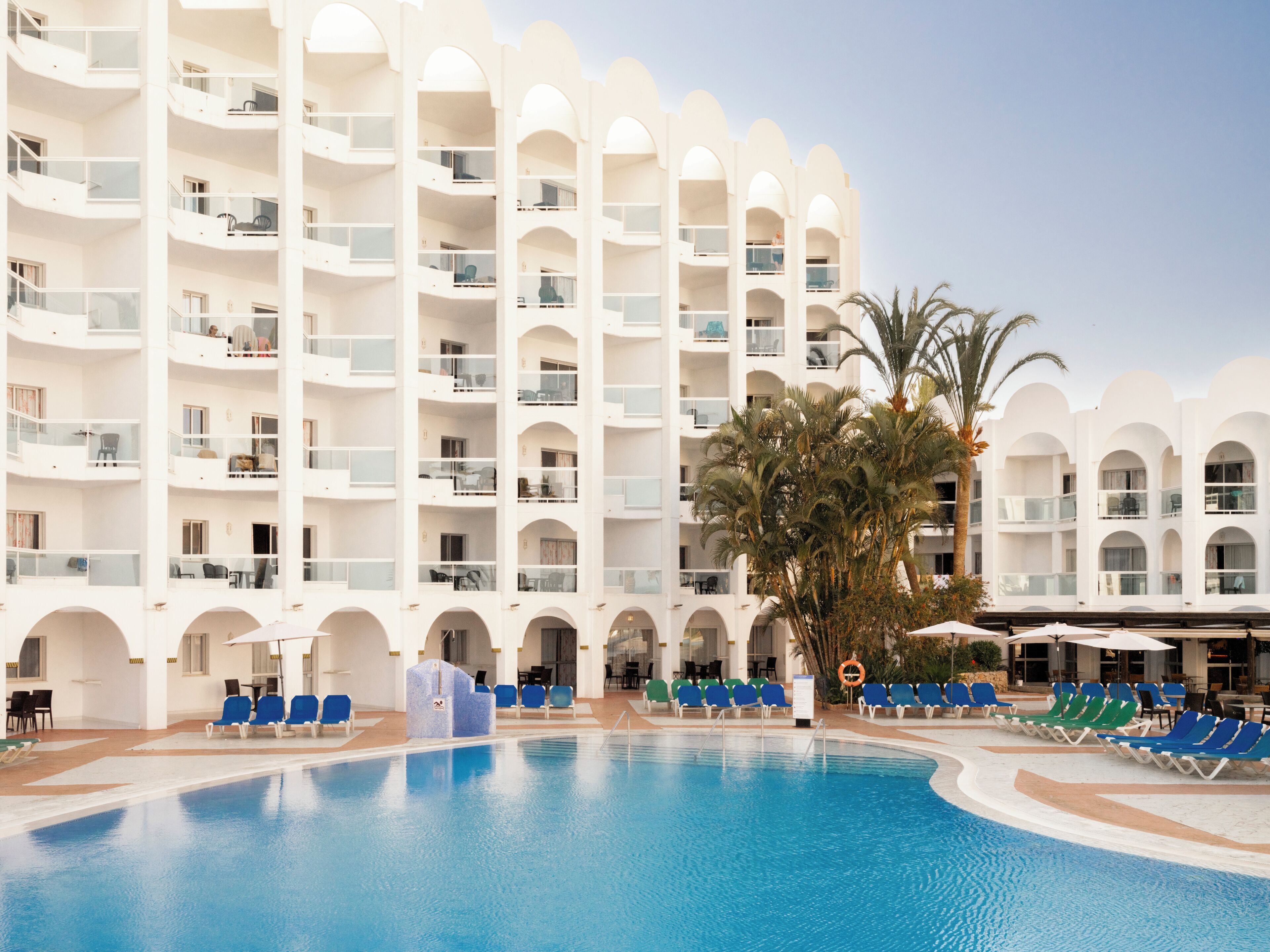 Ein Hotel mit mehreren Balkonen, einem Schwimmbad und Palmen.