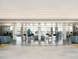 A spacious lobby with a view of the ocean, featuring a seating area with sofas and chairs, a reception desk, and an ATM machine.