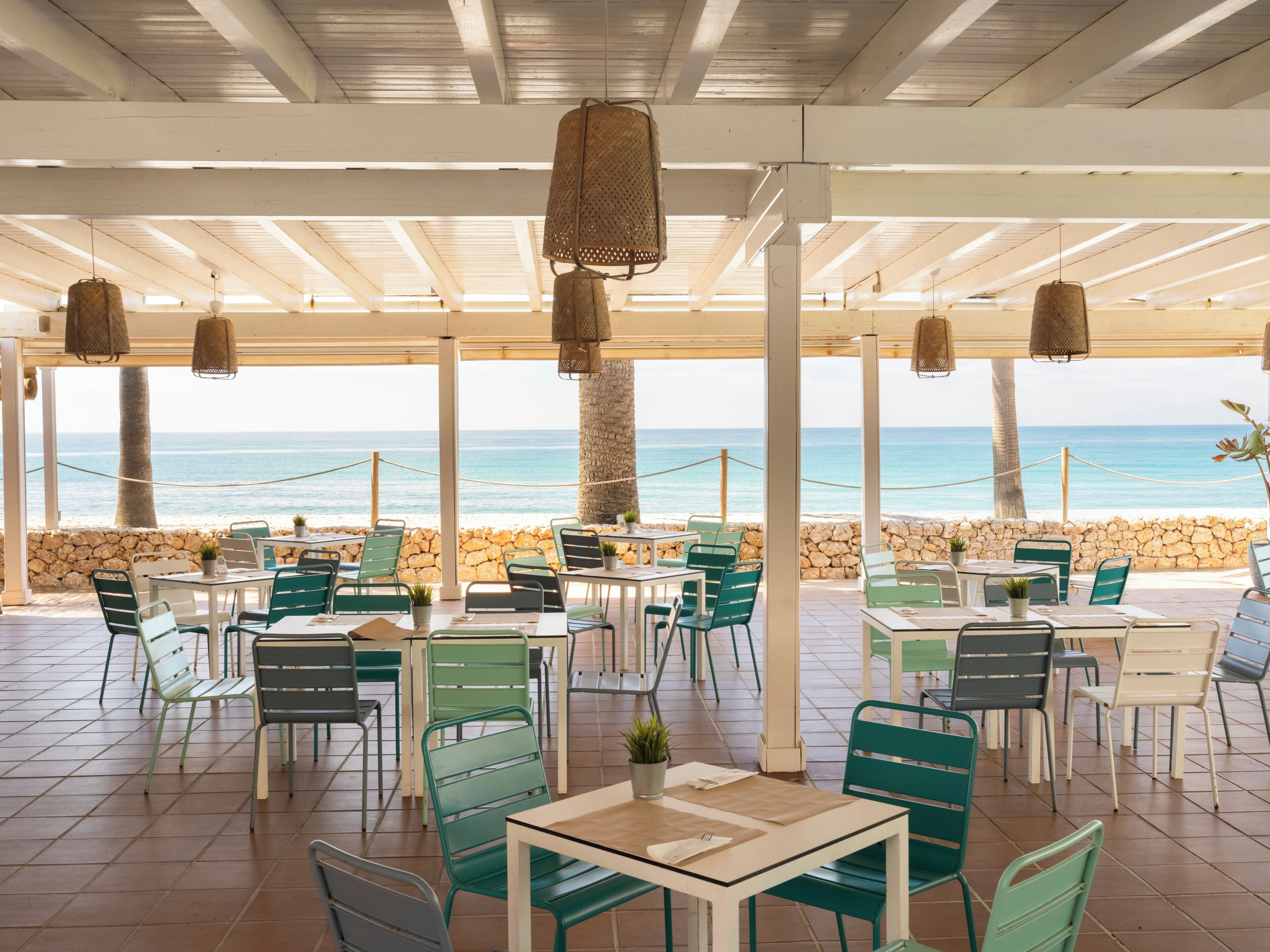 An outdoor seating area with tables and chairs, overlooking a beach.