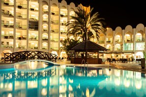 A swimming pool with a bridge, palm trees, and a building with multiple balconies and lights. - Ona Marinas de Nerja Spa Resort (Nerja)