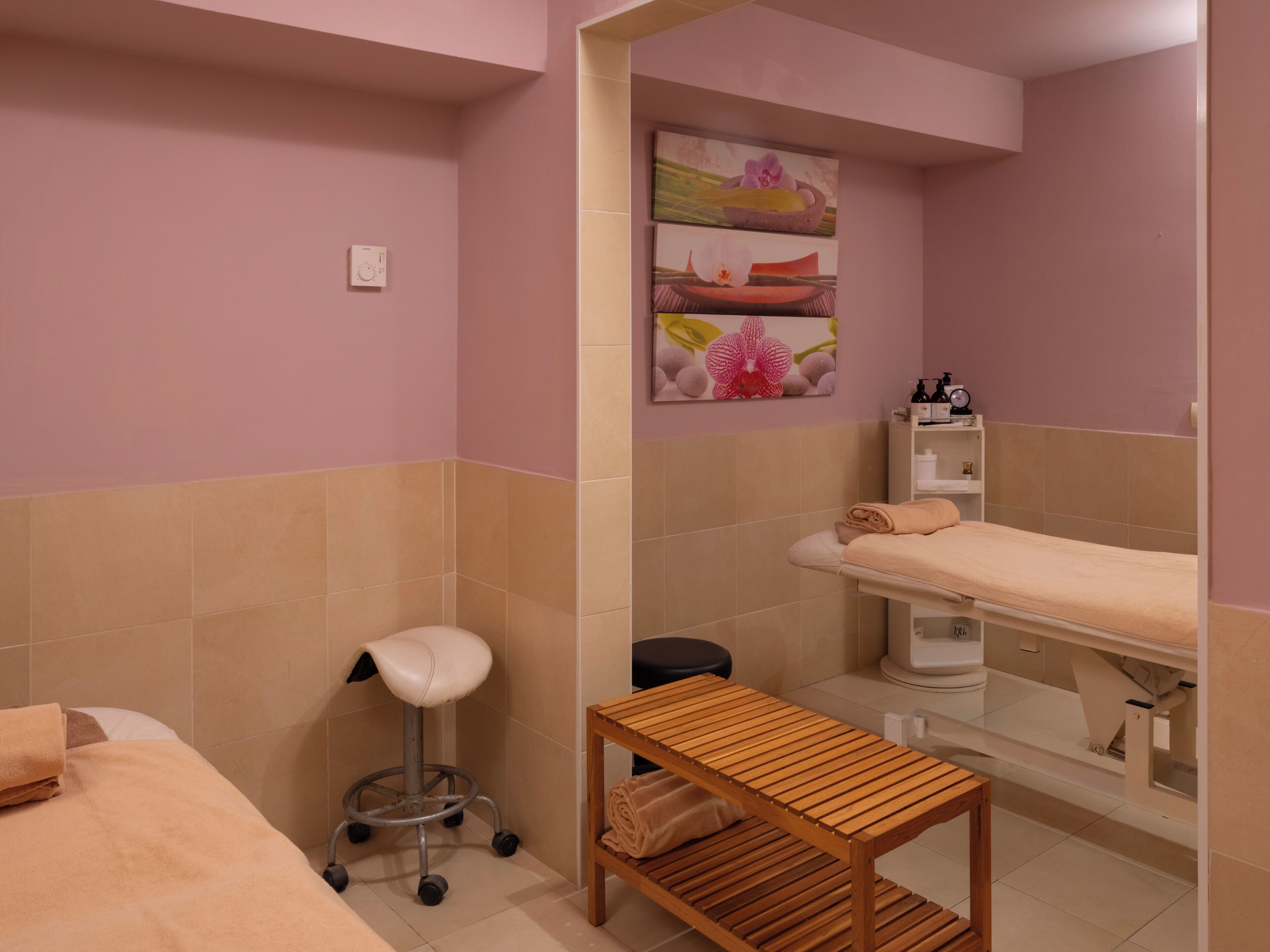 Une salle de spa équipée d’une table de massage, d’un tabouret en bois, d’une petite table en bois et d’une étagère où sont posées des bouteilles.