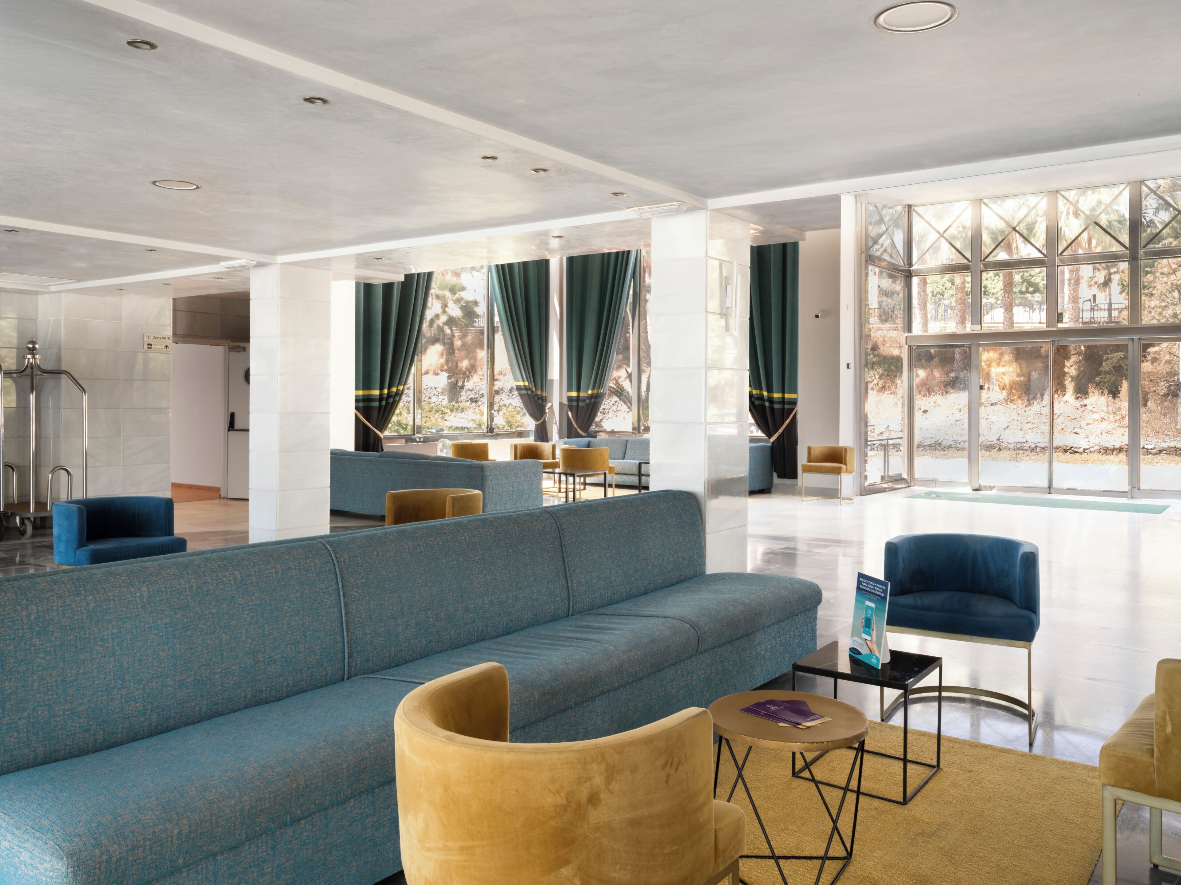 A spacious lobby with a large blue sofa, yellow armchairs, and a coffee table.