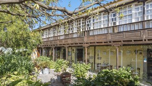 A traditional building with a covered patio area, featuring potted plants and outdoor seating. - Hotel Rural las Calas (Vega de San Mateo)