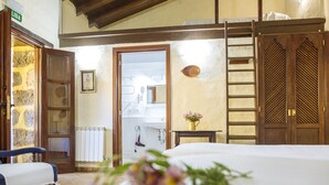 A hotel room with a bed, a wooden wardrobe, a small table with a vase, a chair, and a bathroom visible through an open door. - Hotel Rural las Calas (Vega de San Mateo)