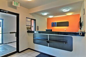A reception area with a reception desk, an exit sign, and a wall-mounted phone. - Ameri Vu Inn (Gilman)