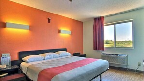 Une chambre d’hôtel avec un lit, des tables de chevet, une fenêtre avec des rideaux et des lampes fixées au mur.