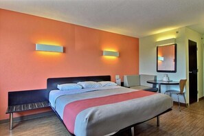 A hotel room with a bed, a desk, a chair, and a wall-mounted TV. - Ameri Vu Inn (Gilman)