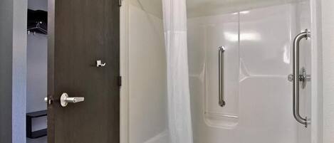 A walk-in shower with a glass door, a showerhead, and a handrail.