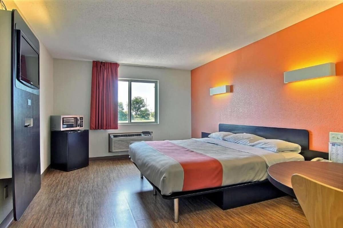 Une chambre d’hôtel équipée d’un lit, d’un bureau, d’une chaise, d’une télévision, d’un radiateur et d’une fenêtre avec des rideaux.