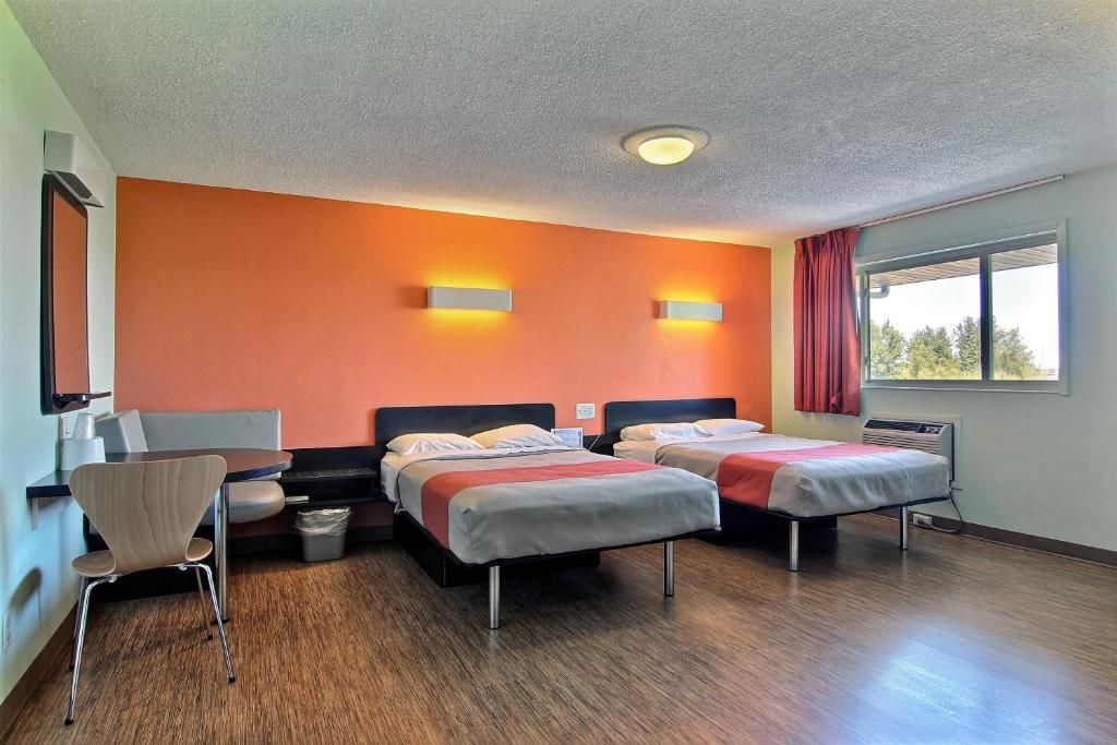 Ein Hotelzimmer mit zwei Betten, einem Schreibtisch, einem Stuhl und einem Fenster mit Vorhängen.