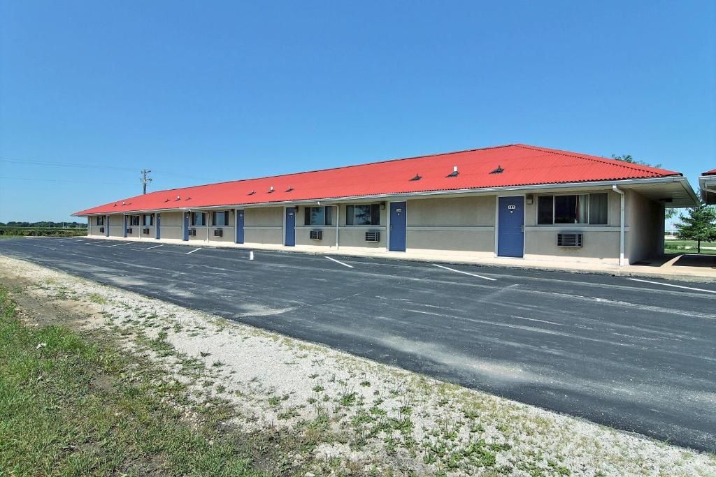 Un motel avec un toit rouge, plusieurs chambres et un parking.