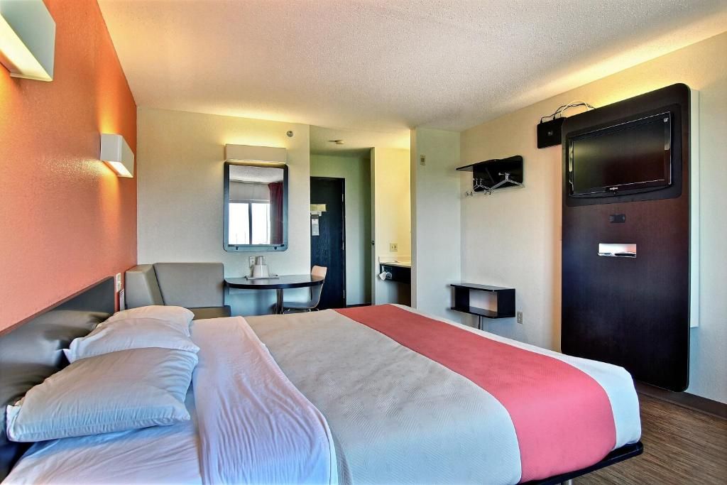Una habitación de hotel con cama, escritorio, silla, televisor y puerta.