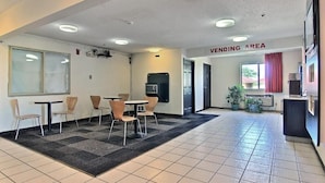 A waiting area with tables and chairs, a vending machine, and a sign indicating a vending area.