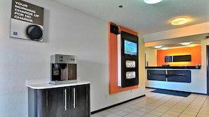 A hotel reception area with a coffee machine, a digital screen, and a counter.
