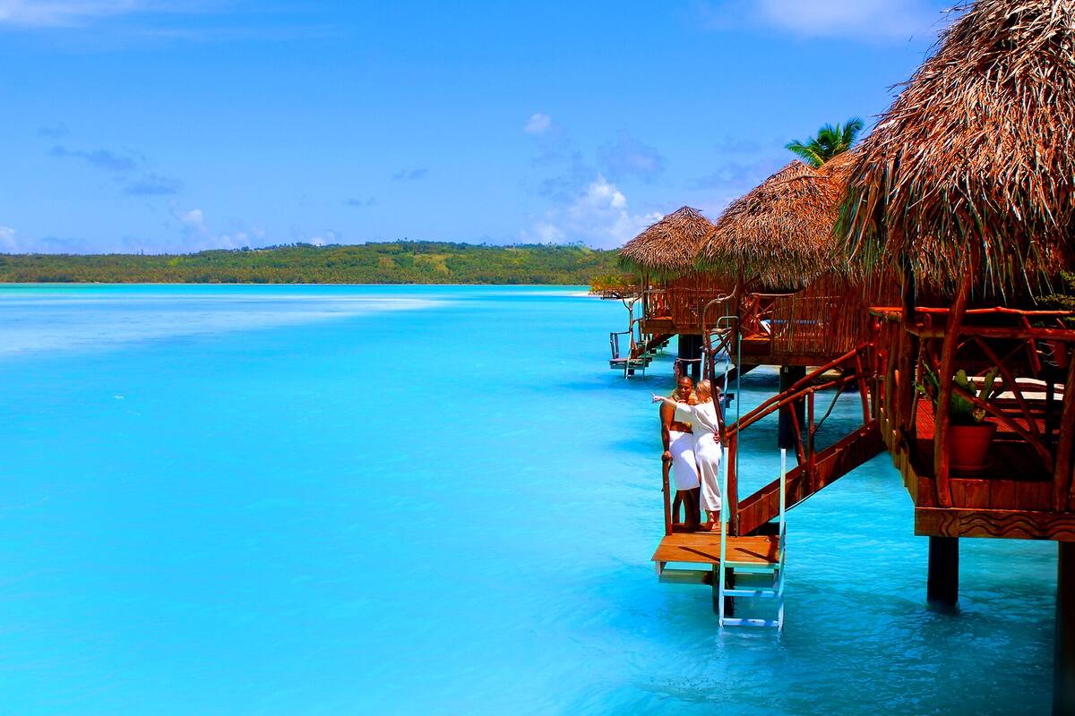 Overwater bungalows with thatched roofs, wooden walkways, and clear turquoise water.