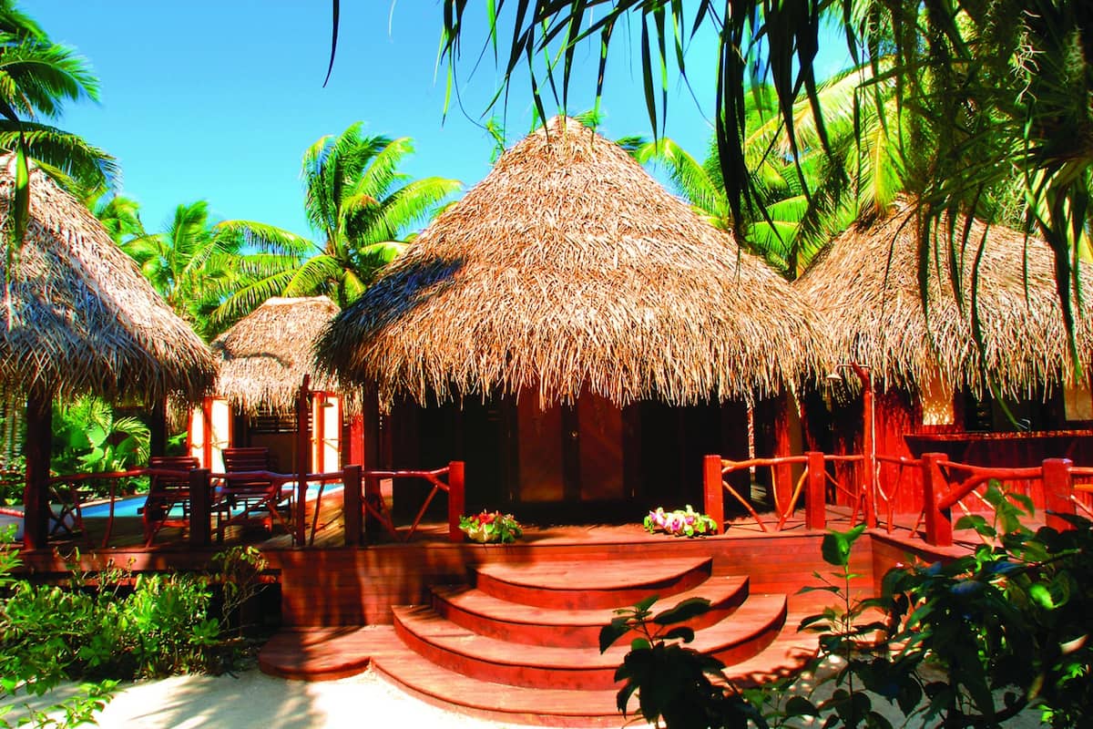 A resort with thatched-roof huts, a pool, and palm trees.