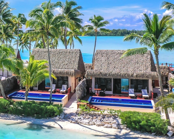 A resort with thatched-roof huts, a pool, and palm trees.