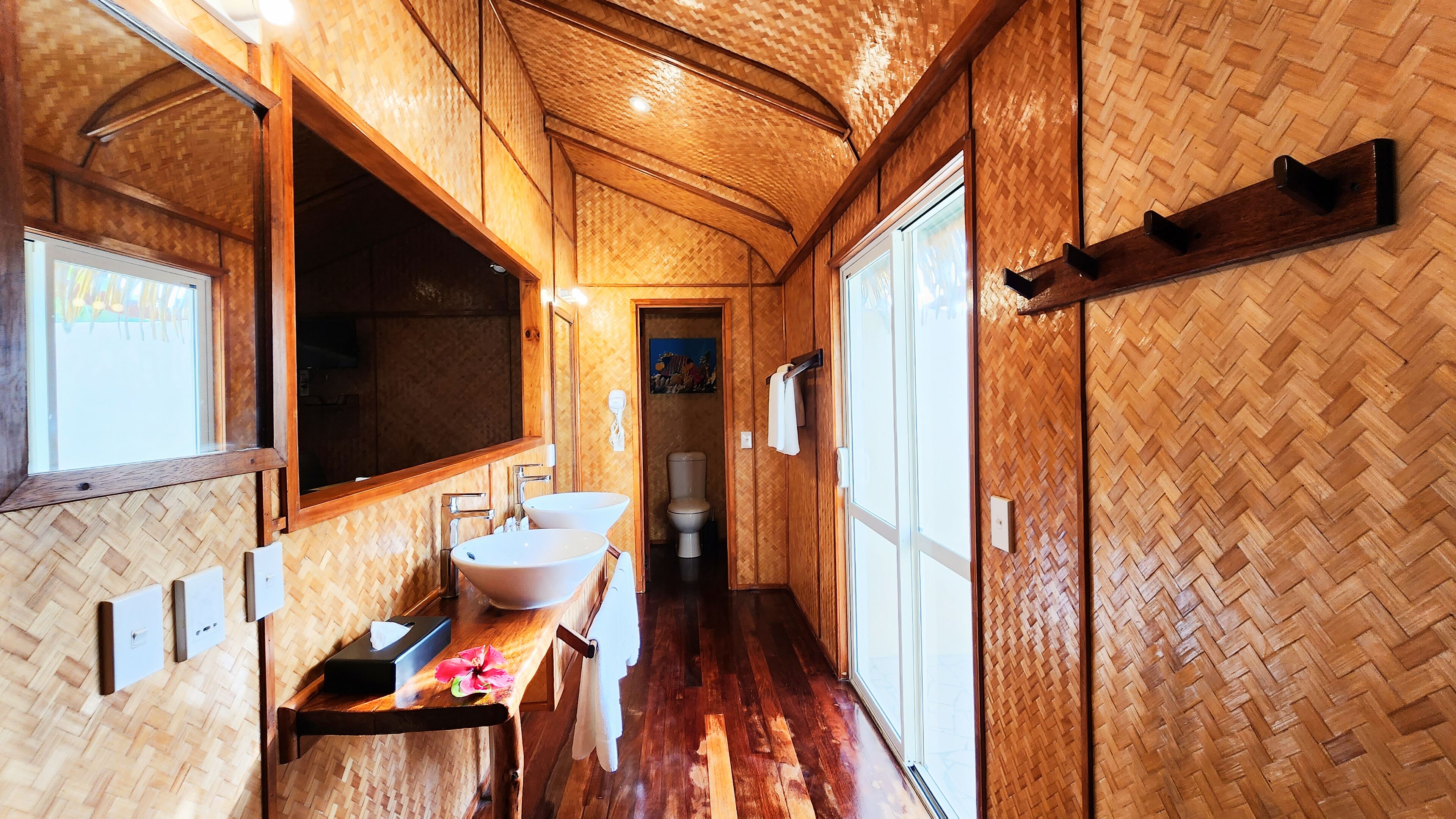 A bathroom with a wooden herringbone floor, a large mirror, two sinks, and a toilet.