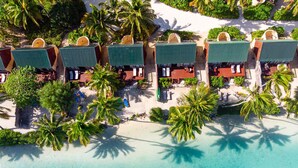 An aerial view of a beach resort with multiple bungalow-style accommodations, each with a private pool and surrounded by palm trees.