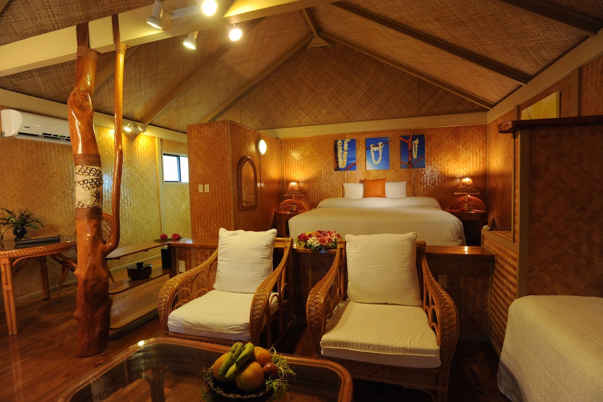 Quarto com uma cama grande, duas cadeiras de madeira, uma mesa de jantar e uma cesta de frutas.