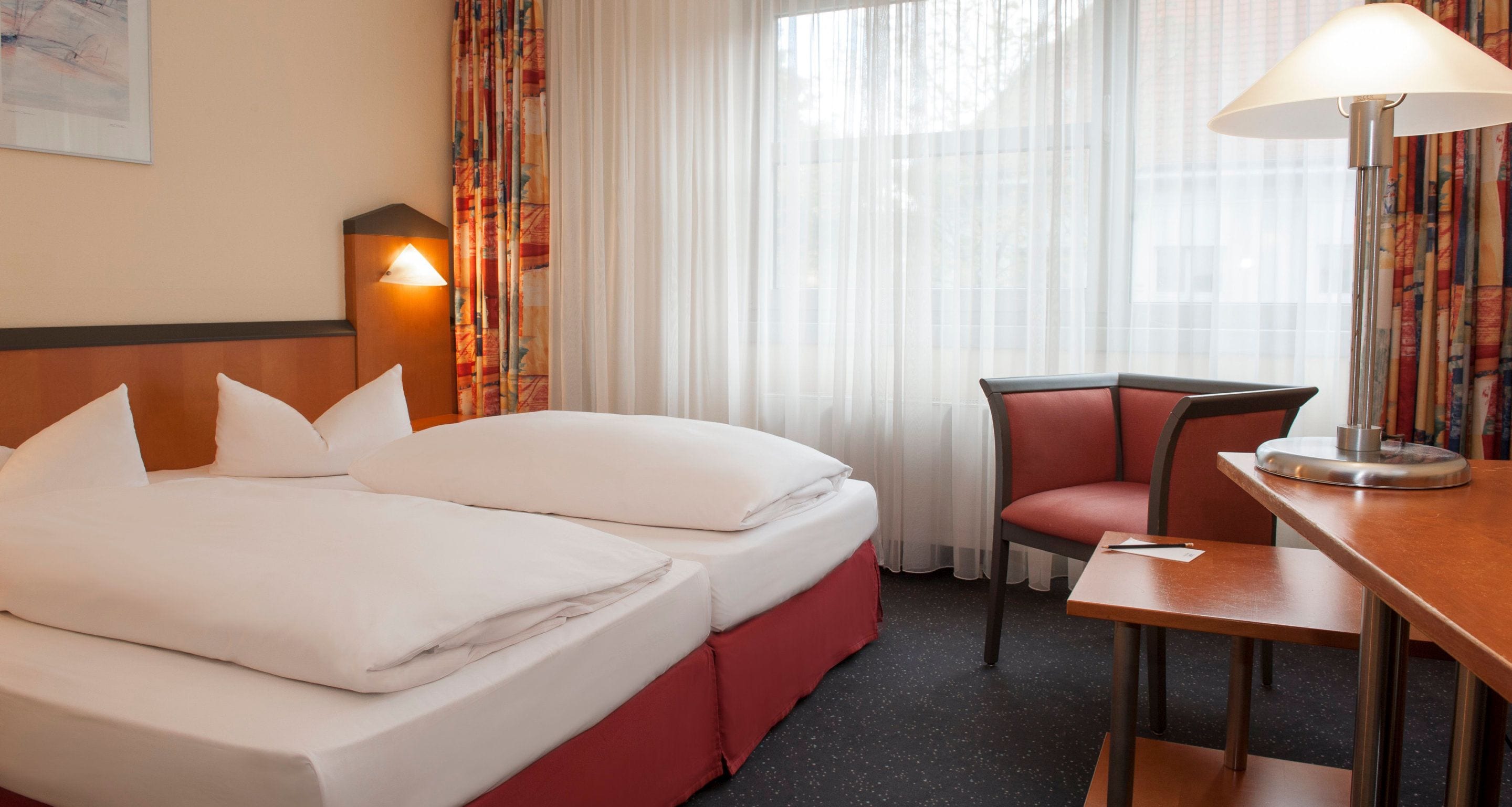 A hotel room with a bed, a desk, a chair, and a lamp.