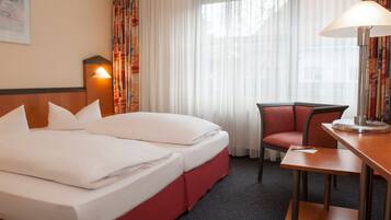 A hotel room with a bed, a desk, a chair, and a lamp.