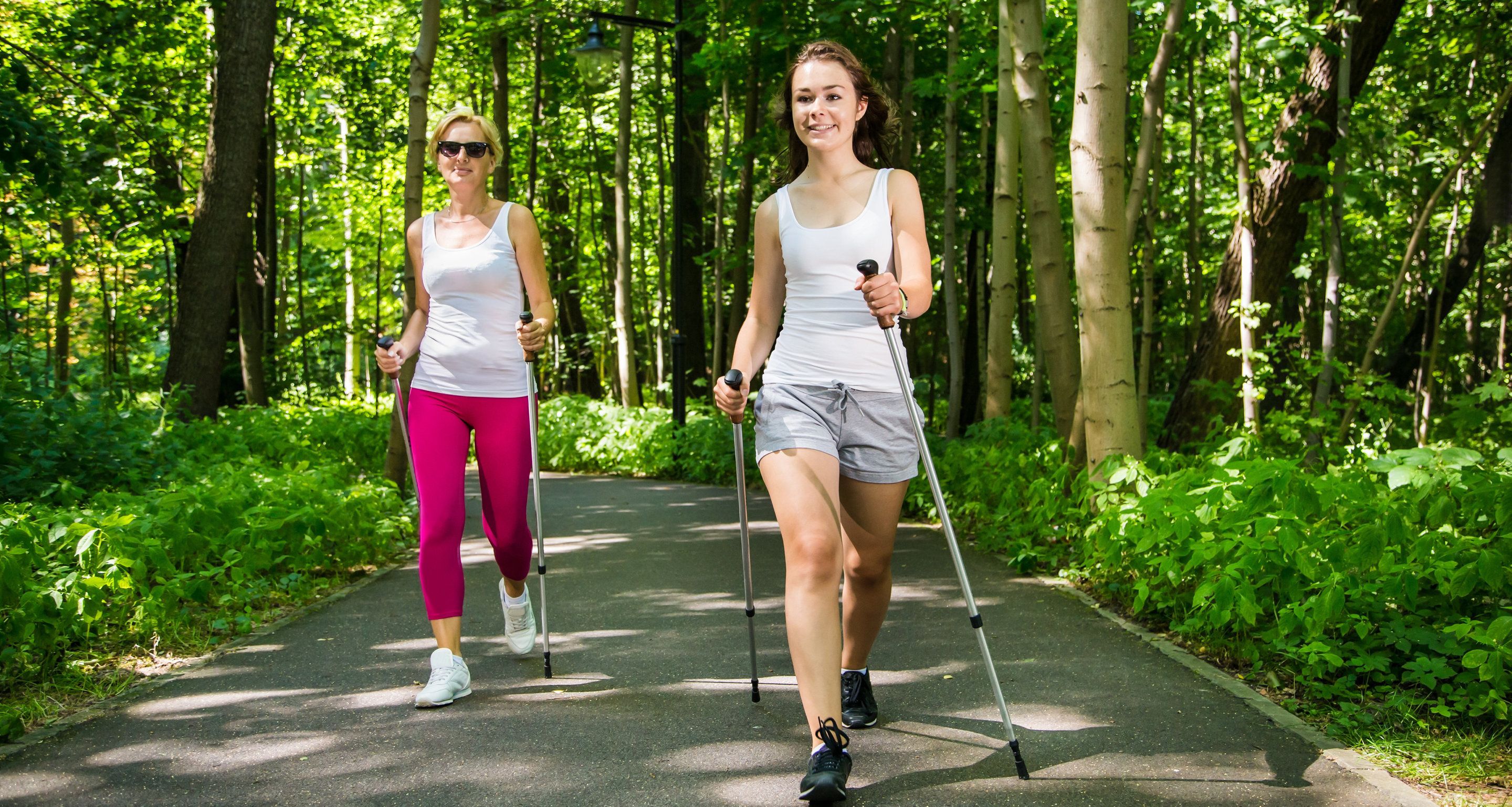 Two people walking on a paved path surrounded by greenery.