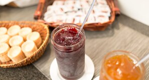 A glass of dark purple juice with a spoon, a basket of sliced bread, and a jar of orange jam on a table. - Victor’s Residenz-Hotel Berlin-Tegel (Berlin)