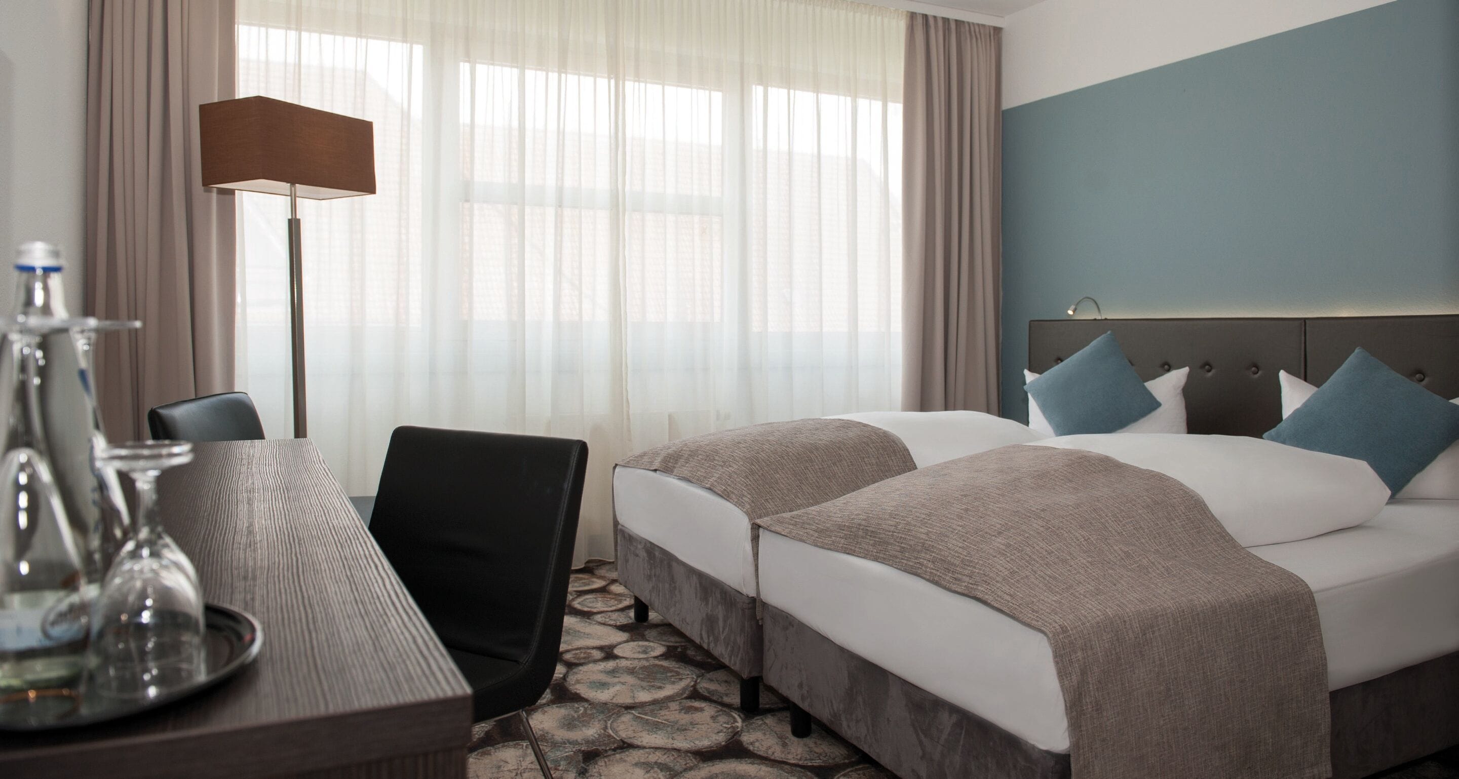 A hotel room with a bed, a desk with a lamp, and a chair.