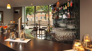 Un espace bar doté d’un comptoir incurvé, de nombreux verres, des bouteilles et offrant une vue sur les bâtiments environnants.