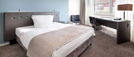 Una habitación de hotel con cama, escritorio, silla y ventana con cortinas.